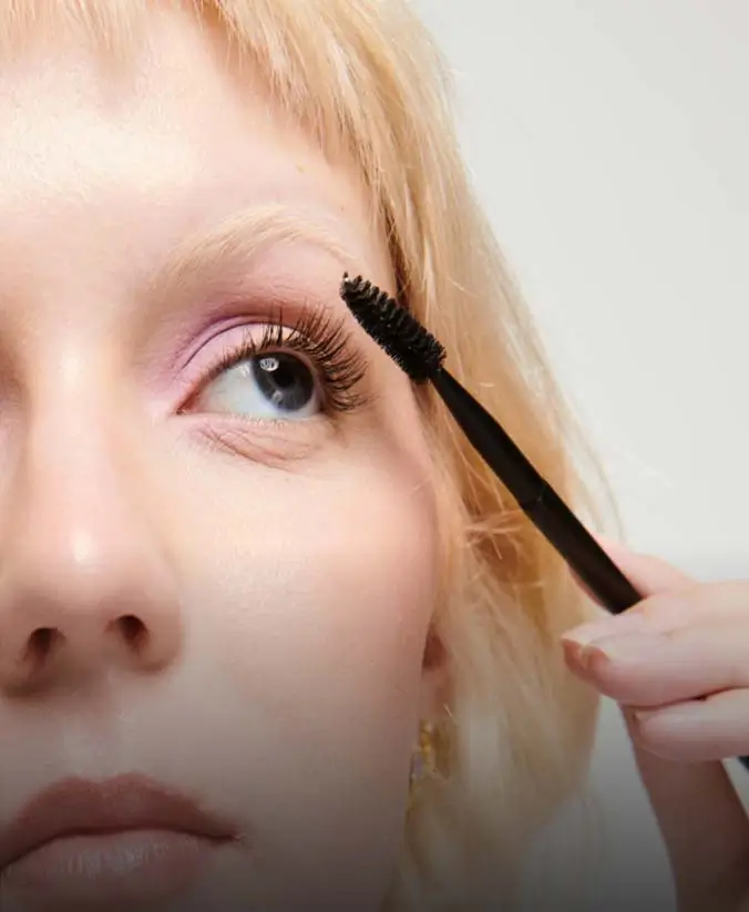 woman applying mascara to her eye lashes